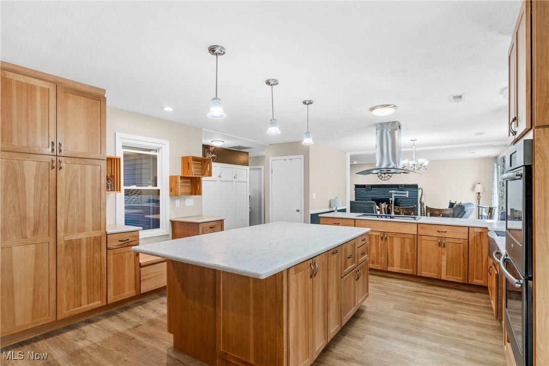 7944 Middle Ridge Road Madison, OH 44057 - Photo 6 of 31 Kitchen featuring hanging light fixtures, a center island, light wood-style floors, island range hood, and brown cabinets