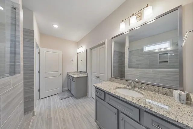 a bathroom with a granite countertop double vanity sink a mirror and a shower