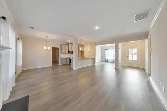 a view of an empty room and a kitchen with wooden floor