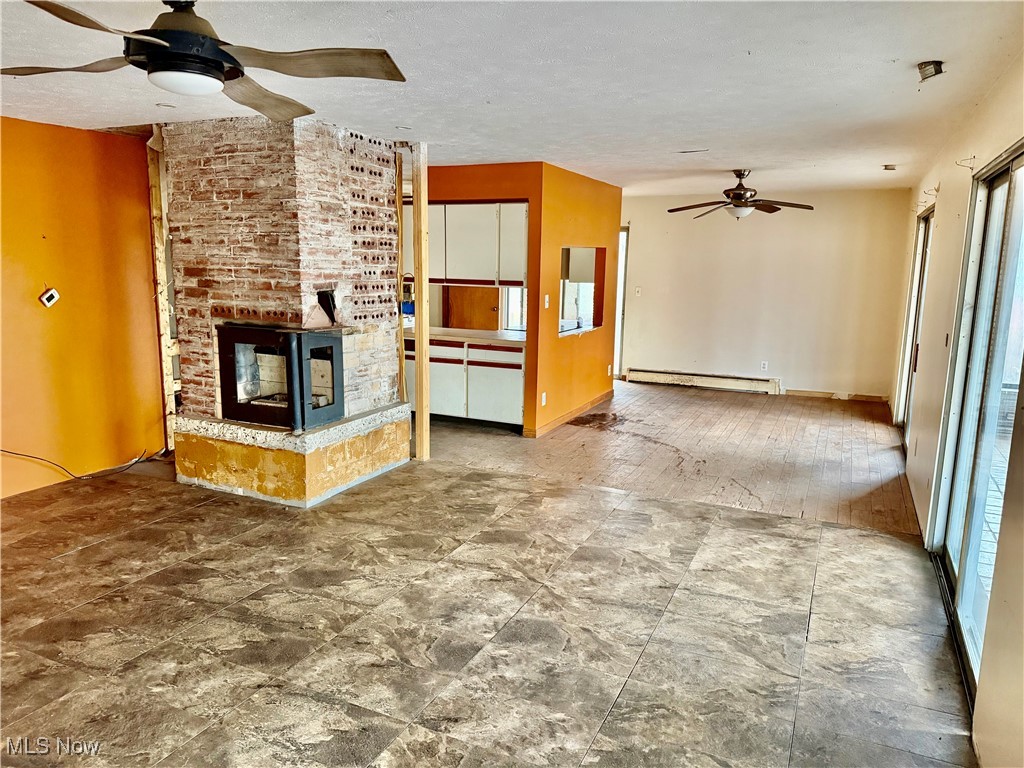 2898 Canton Road Uniontown, OH 44685 - Photo 8 of 20 Unfurnished living room with ceiling fan, a fireplace, a baseboard heating unit, and a textured ceiling