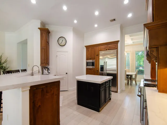 a large kitchen with a large counter top a sink a refrigerator and wooden floor