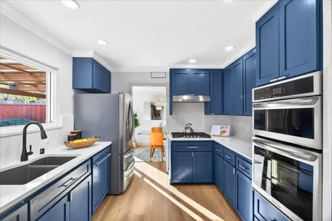 a kitchen with stainless steel appliances a sink a stove a refrigerator cabinets and a window