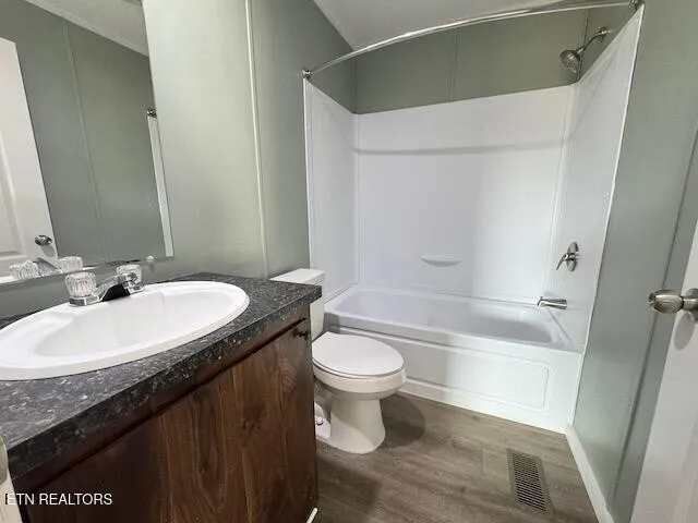 a view of empty room with wooden floor and kitchen