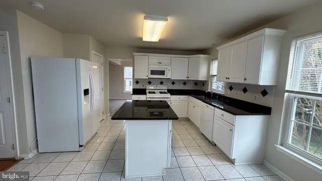 a kitchen with granite countertop a refrigerator a sink and white cabinets