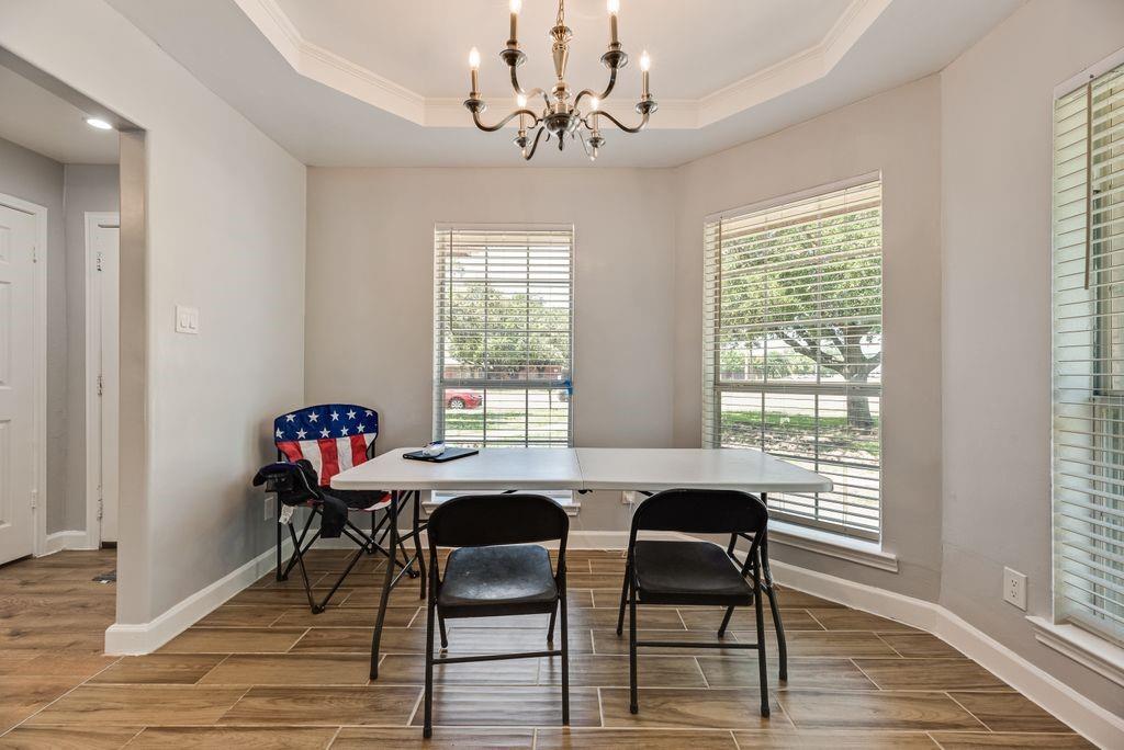 5114 Ben Davis Road Sachse, TX 75048 - Photo 7 of 28 Dining area featuring wood-finish tile flooring, a tray ceiling with crown molding, and a black chandelier