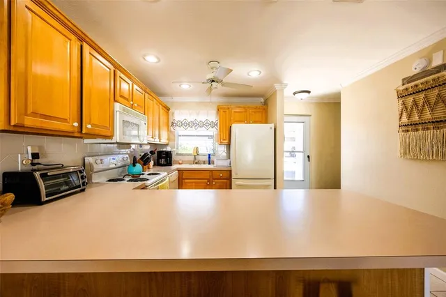 a large white kitchen with stainless steel appliances granite countertop a refrigerator a stove and a view of living room