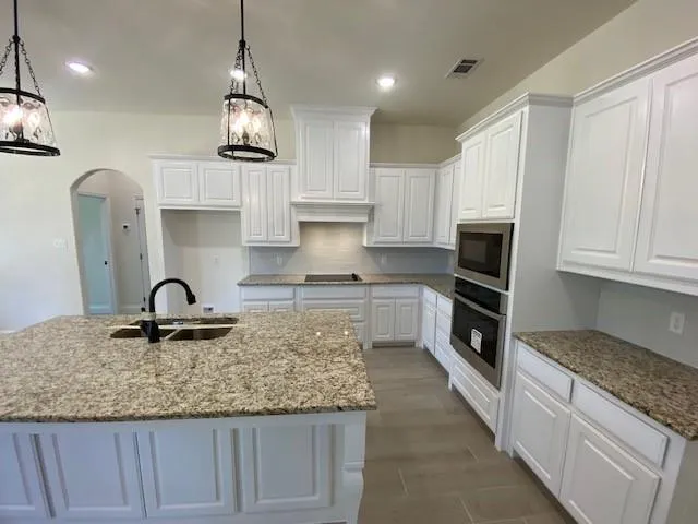 a kitchen with kitchen island granite countertop a stove a sink a refrigerator and white cabinets with wooden floor