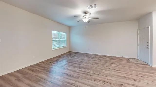 a view of an empty room with wooden floor and a window