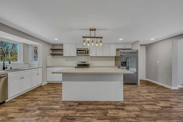 a large kitchen with kitchen island a sink wooden floor and stainless steel appliances