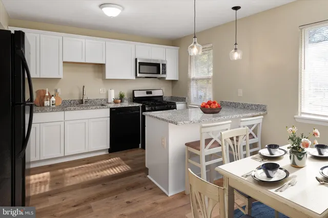 a kitchen with stainless steel appliances granite countertop a stove a sink dishwasher a refrigerator and white cabinets with wooden floor