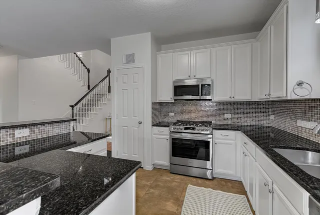 a kitchen with granite countertop a sink dishwasher stove and oven with cabinets