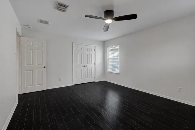 an empty room with wooden floor ceiling fan and windows