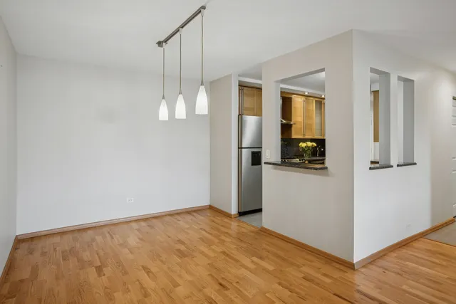 a view of empty room with wooden floor and kitchen