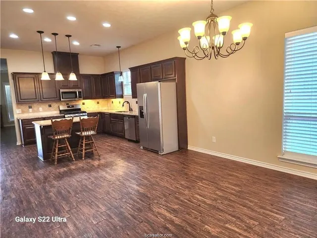 a kitchen with stainless steel appliances granite countertop a refrigerator a stove top oven a sink dishwasher and a dining table with wooden floor