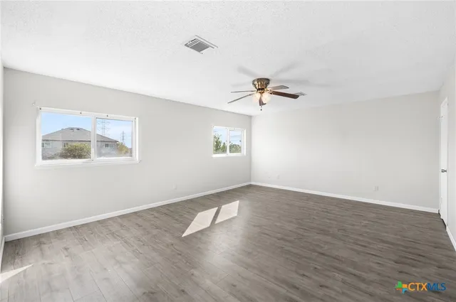 an empty room with wooden floor chandelier fan and windows