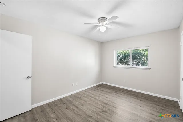 an empty room with wooden floor fan and windows