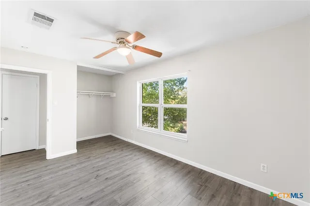 an empty room with wooden floor chandelier fan and windows