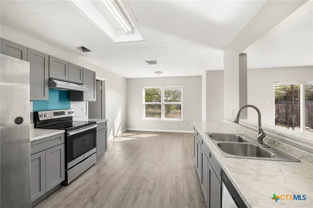 a kitchen with stainless steel appliances granite countertop a sink a stove a refrigerator cabinets and a window