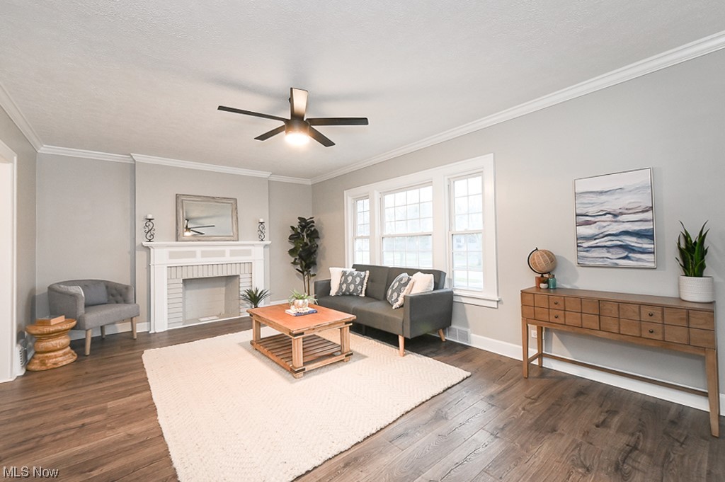Living room featuring dark hardwood / wood-style floors, a brick fireplace, ceiling fan, and crown molding