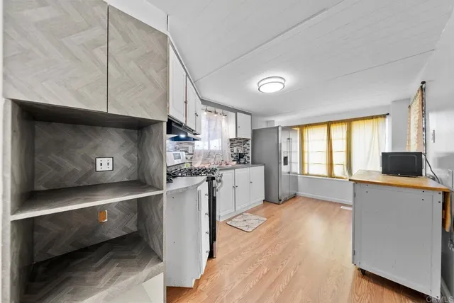 a kitchen with stainless steel appliances a stove a sink a refrigerator white cabinets and wooden floor