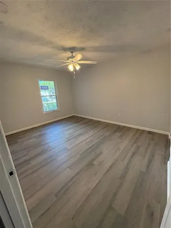 an empty room with wooden floor chandelier fan and windows