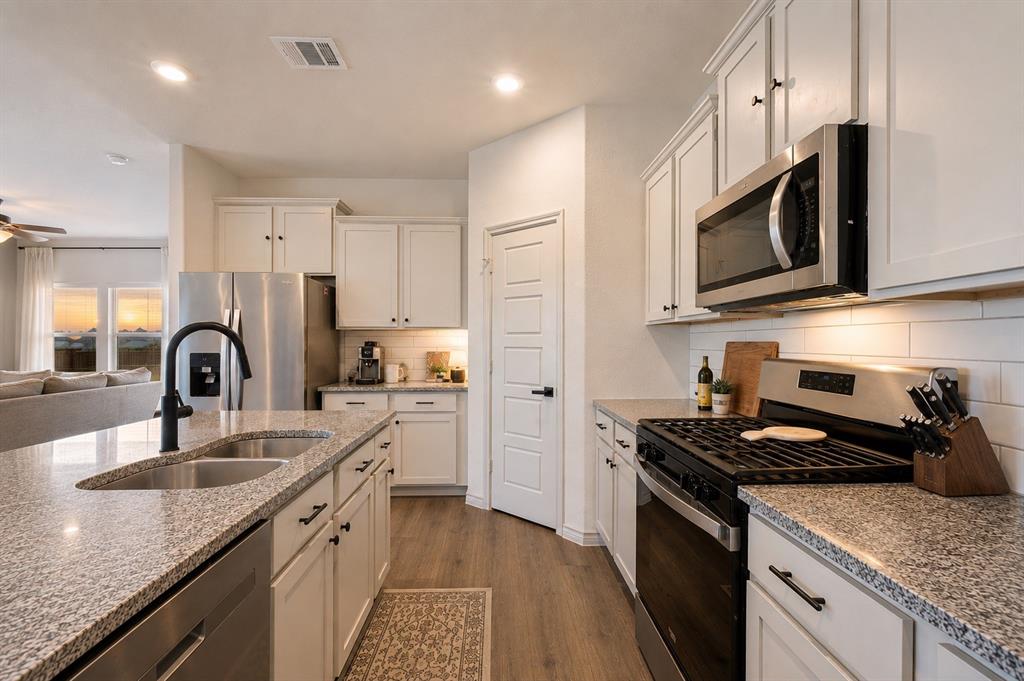 9828 Quail Pointe Road Aubrey, TX 76227 - Photo 5 of 23 Kitchen featuring white cabinetry, granite countertops, stainless steel appliances, a subway tile backsplash, and wood-finish flooring