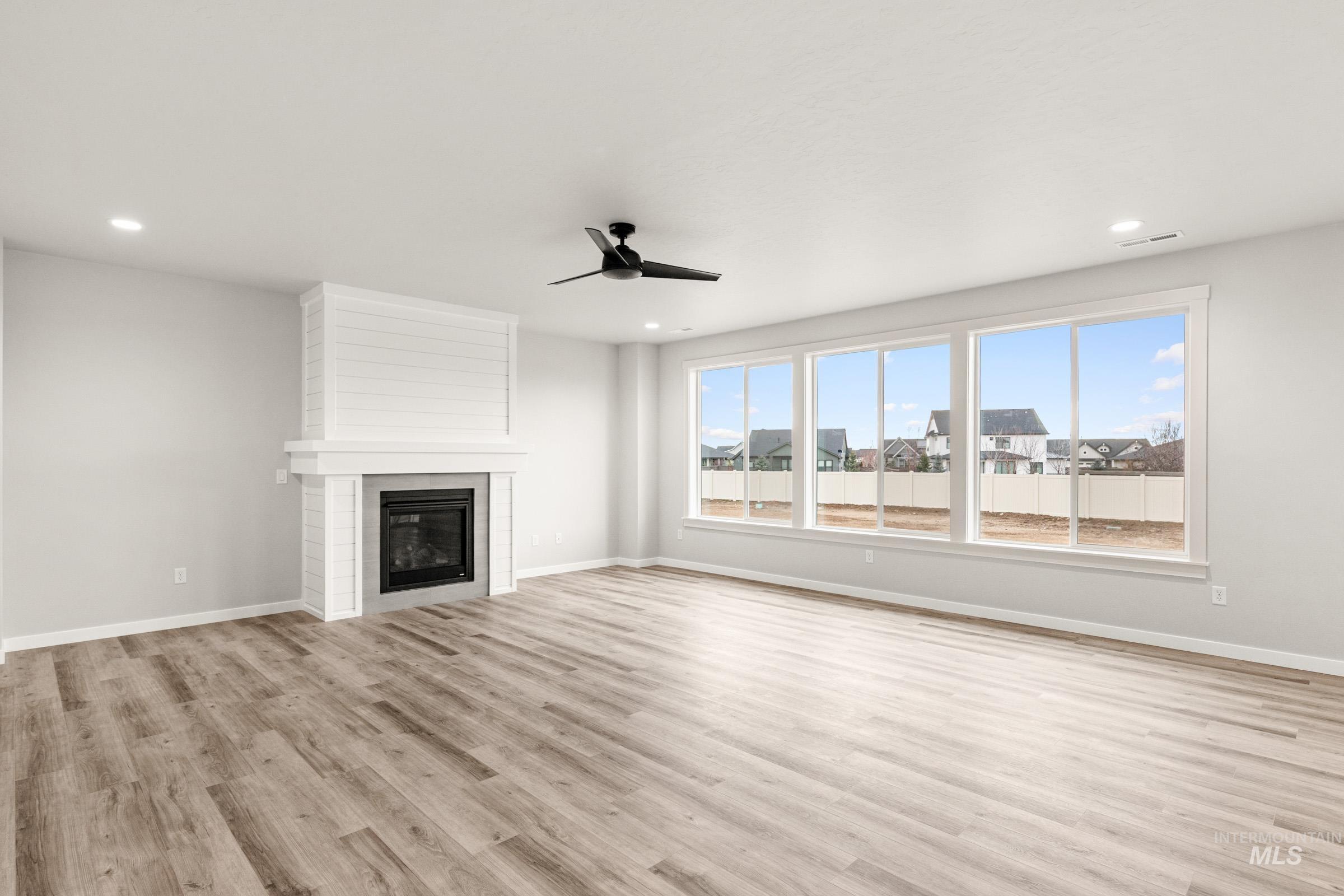 4227 East Rincon Drive Meridian, ID 83642 - Photo 12 of 31 Expansive living area featuring a fireplace with shiplap detailing, a modern black ceiling fan, wood-finish flooring, and large picture windows