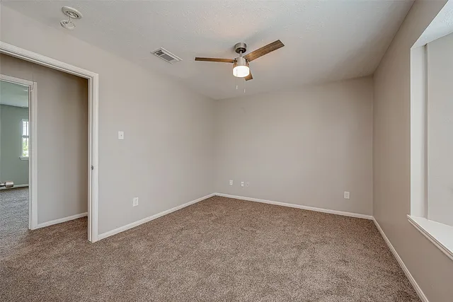 an empty room with chandelier fan and windows