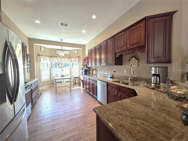 a kitchen with stainless steel appliances granite countertop a refrigerator a sink dishwasher a stove and a refrigerator with wooden floor