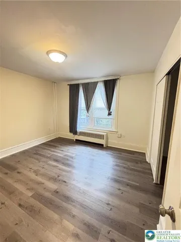 an empty room with wooden floor and exposed radiator