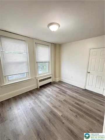 an empty room with wooden floor cabinet and windows