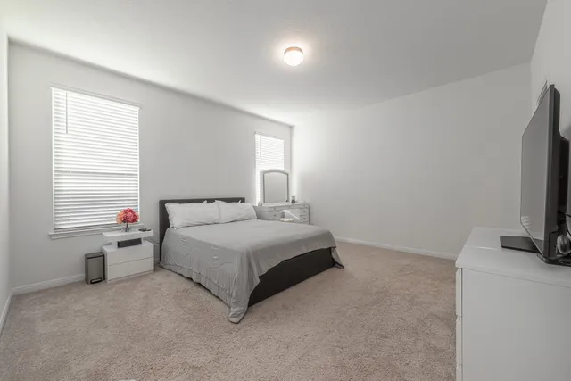 a white bed sitting in a bedroom next to a window with a flat tv screen and a dresser