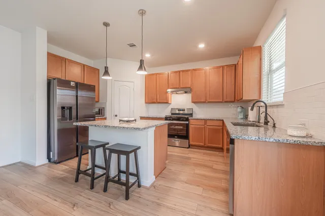 a kitchen with stainless steel appliances granite countertop a sink a stove a refrigerator and island with wooden floor