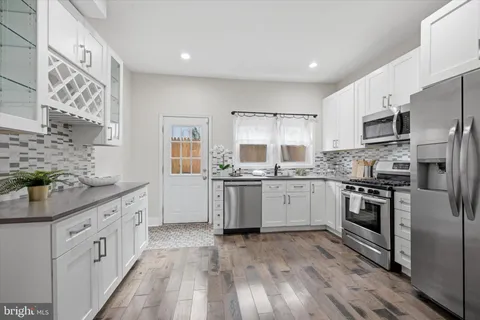 a kitchen with stainless steel appliances granite countertop white cabinets a refrigerator a sink a stove and a wooden floors