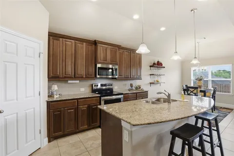 a kitchen with kitchen island granite countertop a table chairs sink and cabinets