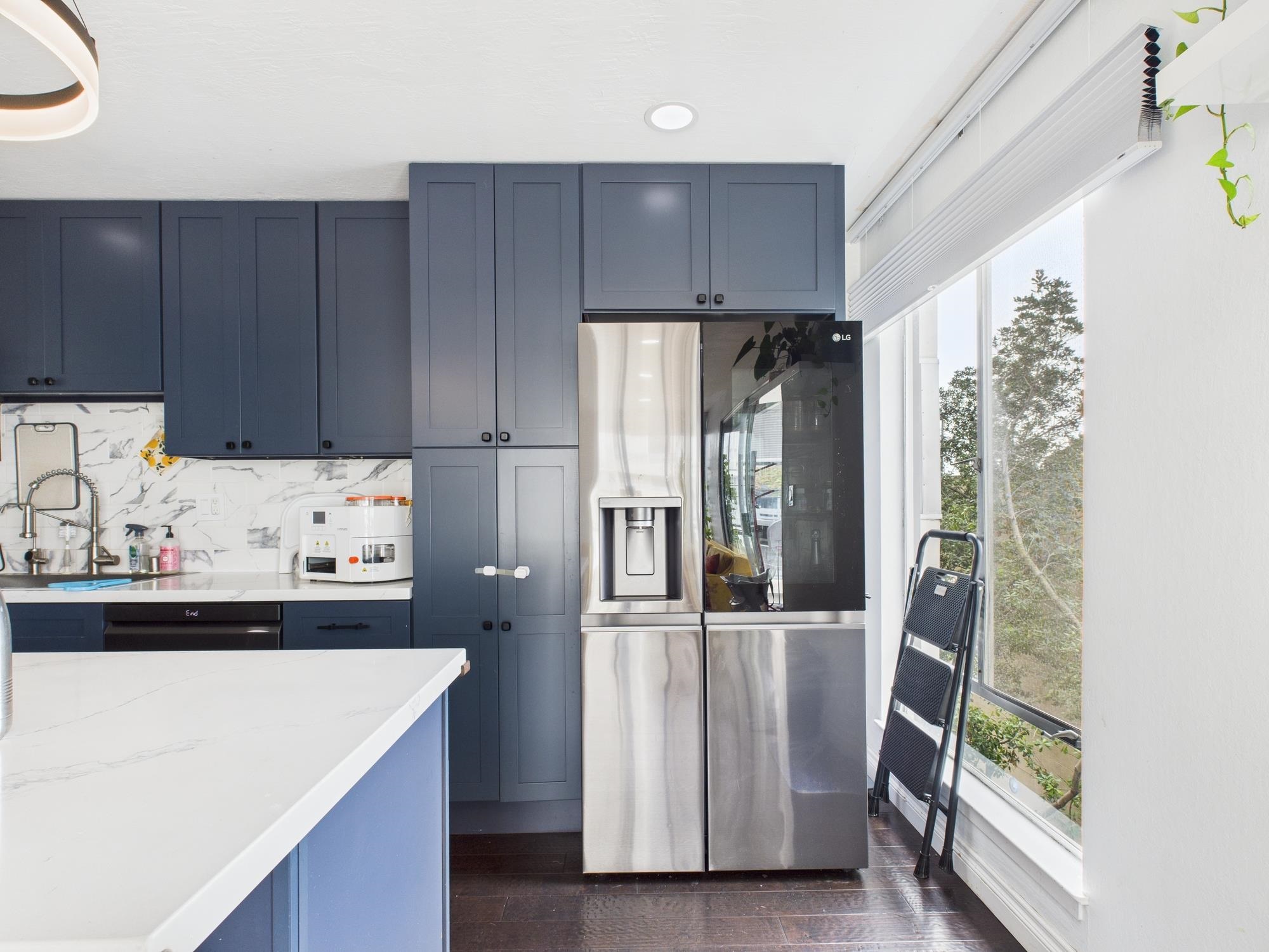 4099 Howe Street, Unit 202 Oakland, CA 94611 - Photo 12 of 19 Kitchen featuring stainless steel fridge, blue cabinets, dark wood-style flooring, light stone counters, and backsplash
