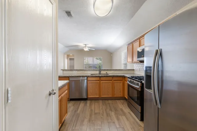 a kitchen with stainless steel appliances granite countertop a refrigerator a sink dishwasher a stove with wooden cabinets and floor