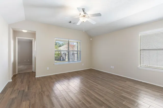 an empty room with wooden floor chandelier fan and windows