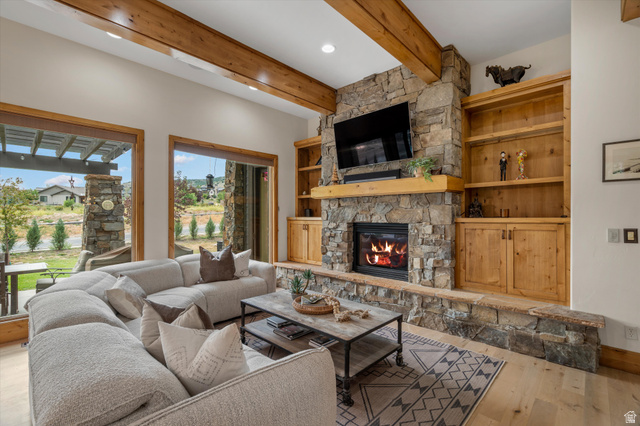 4892 Eagle Rdg Drive Eden, UT 84310 - Photo 3 of 39 Living area featuring a stone fireplace with a wood mantle, built-in shelving, wood-finish flooring, exposed wood beams, and expansive windows