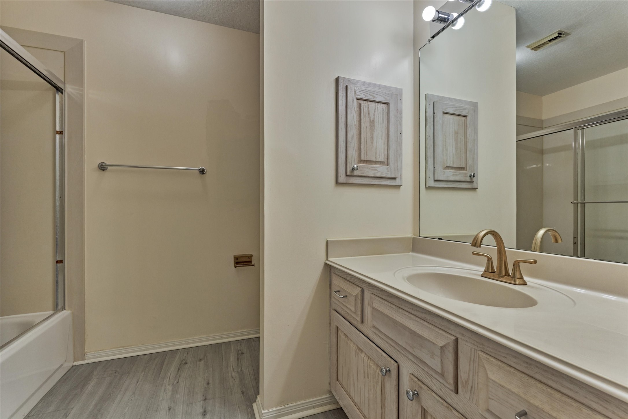 14420 Walters Road, Unit 26 Houston, TX 77014 - Photo 34 of 45 This bathroom features a spacious vanity with a sleek countertop and modern faucet. It has ample storage with wooden cabinets and a large mirror. The room includes a shower / bathtub combo with a sliding glass door and neutral wall tones, providing a clean and functional space.