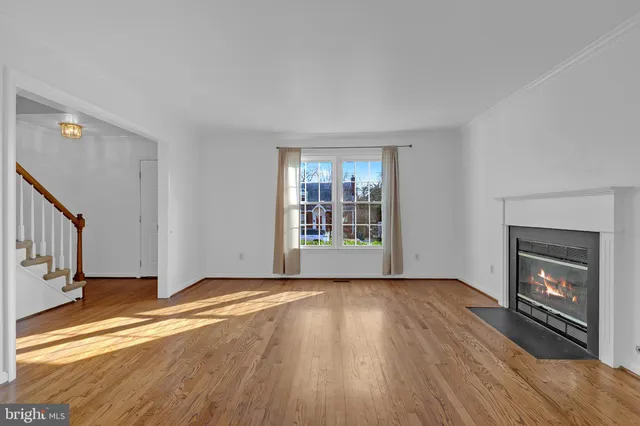 a view of an empty room with wooden floor fireplace and a window