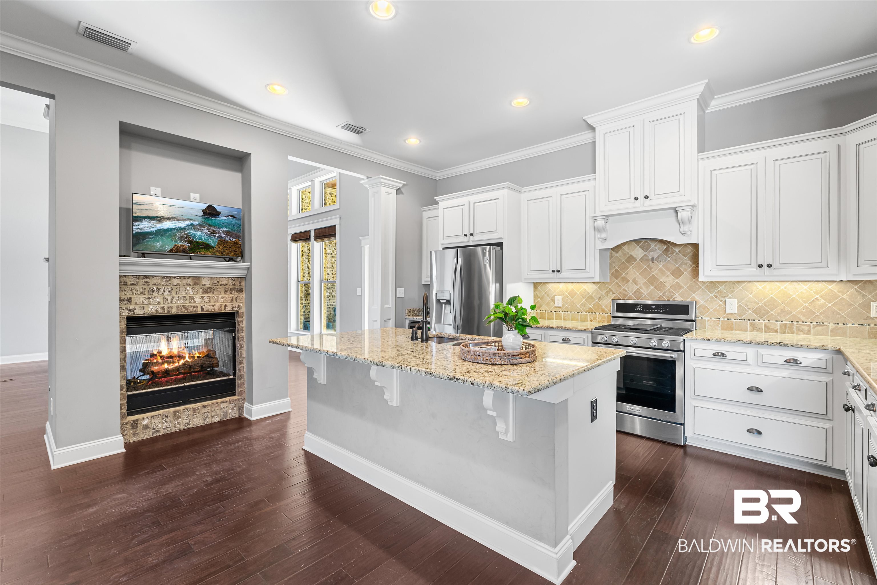 8844 Rosedown Lane Daphne, AL 36526 - Photo 6 of 24 Kitchen with white cabinets, light stone countertops, a multi sided fireplace, an island with sink, and ornamental molding