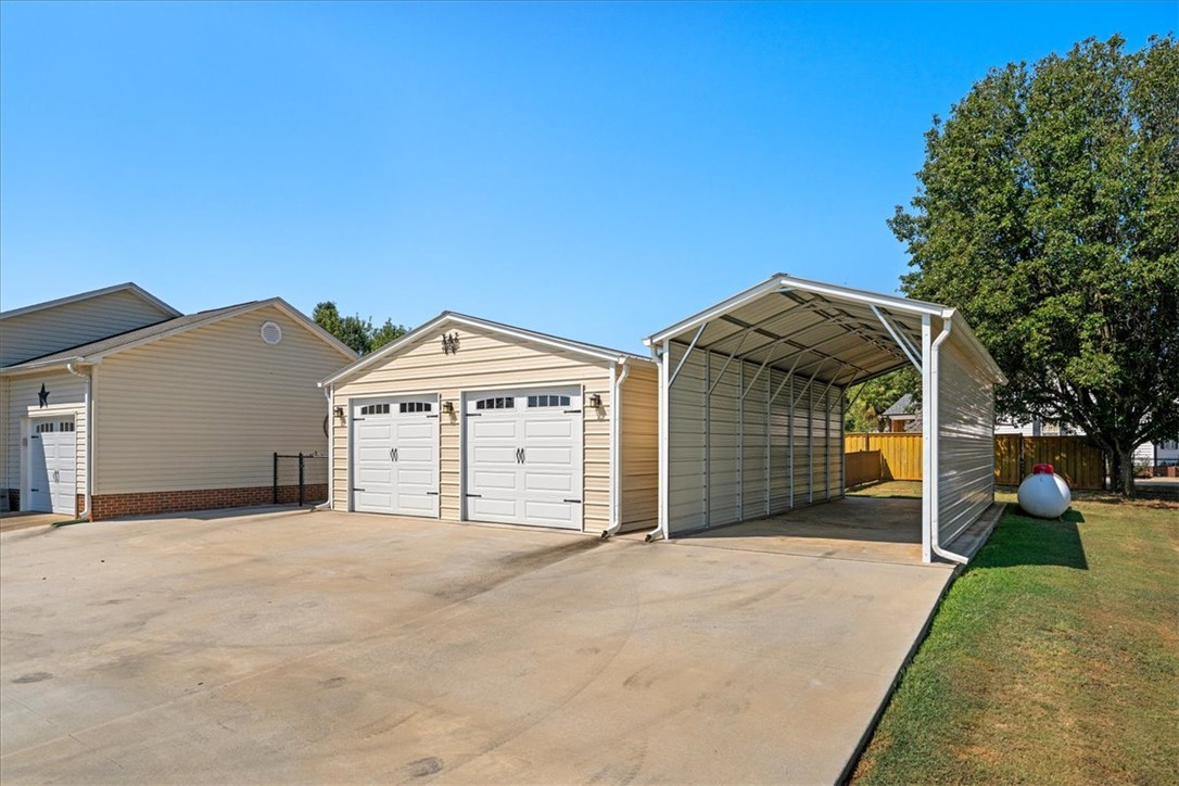 A spacious concrete driveway leads to both a detached garage and a covered carport.
