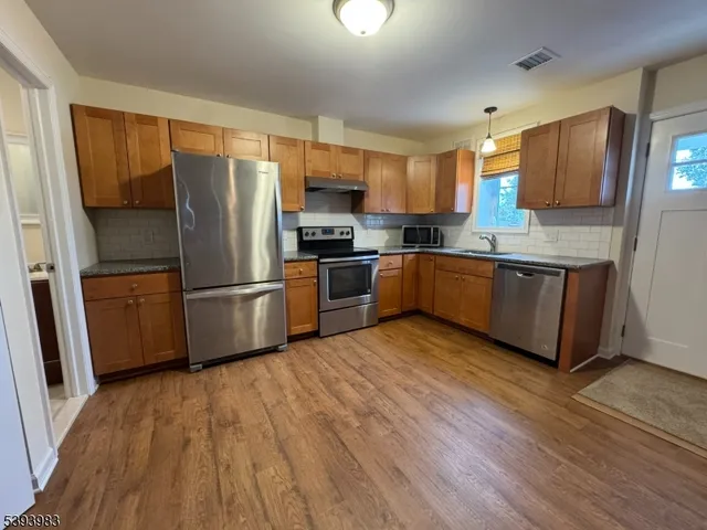 a kitchen with wooden floors stainless steel appliances a sink and a window
