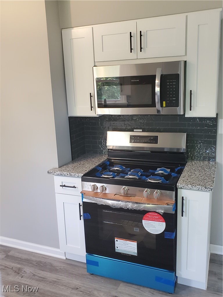 7007 Biddulph Road Brooklyn, OH 44144 - Photo 6 of 16 Kitchen with stainless steel range oven, light wood finished floors, baseboards, white cabinets, and light stone countertops