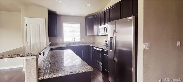 a kitchen with granite countertop a refrigerator a sink and white cabinets
