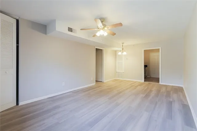 a view of an empty room with wooden floor and a ceiling fan