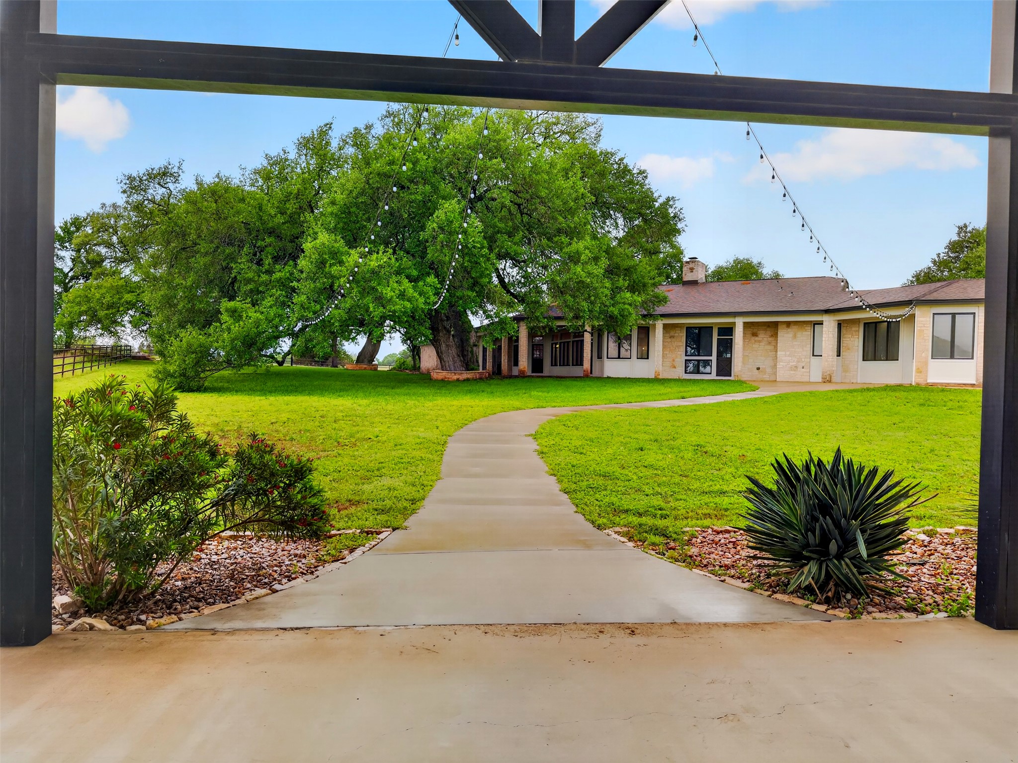 6106 Southeast Fm Ranch Buckholts, TX 76518 - Photo 35 of 38 The property features an extensive lawn with mature trees, a winding concrete pathway, and a single-story building with a brown roof and stone accents