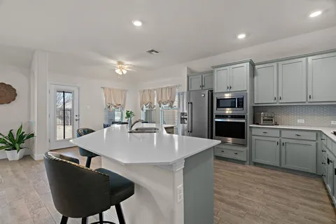 a kitchen with stainless steel appliances kitchen island granite countertop a refrigerator a stove a sink dishwasher and white cabinets with wooden floor