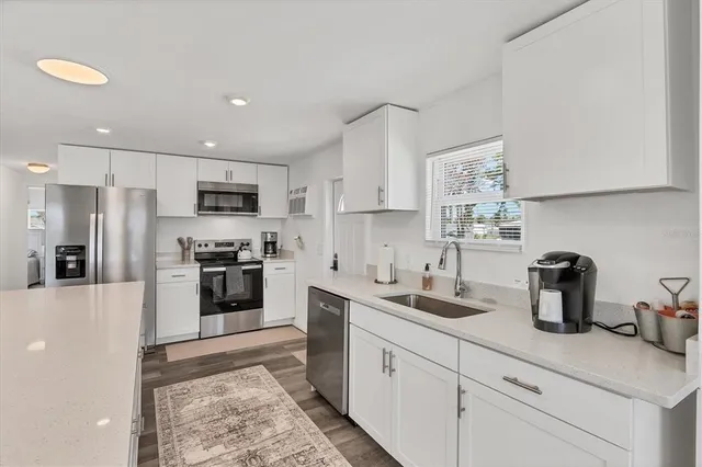 a kitchen with stainless steel appliances kitchen island granite countertop a dining table chairs and a refrigerator
